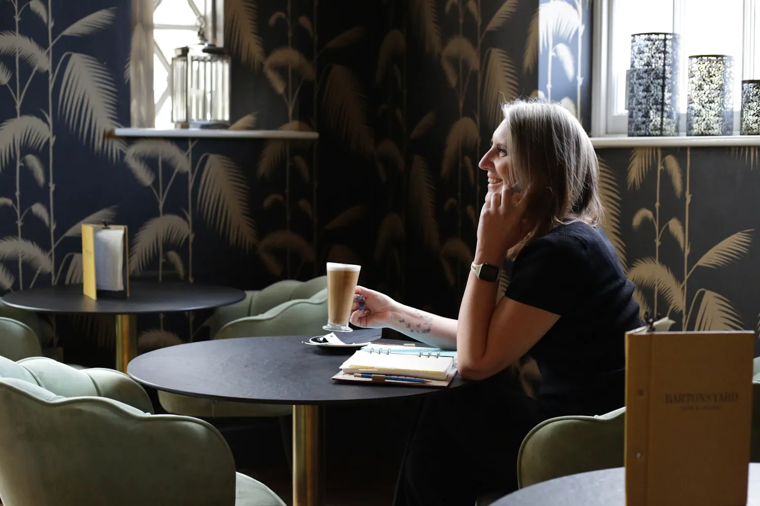 Image of Laura talking on her mobile phone whilst sat in cafe with a coffee in front of her. 